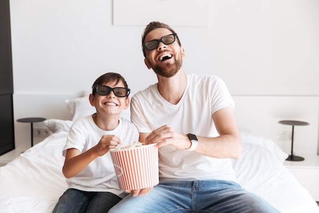 3Dメガネをかけてポップコーンを食べてテレビを見ている息子と一緒に男の父のお父さん。