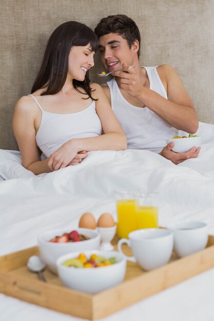 Man feeding breakfast cereals to woman in bedroom