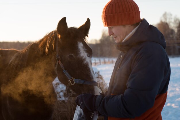 凍るような冬の晴れた日に田舎の農場や牧場で馬に餌をやる男