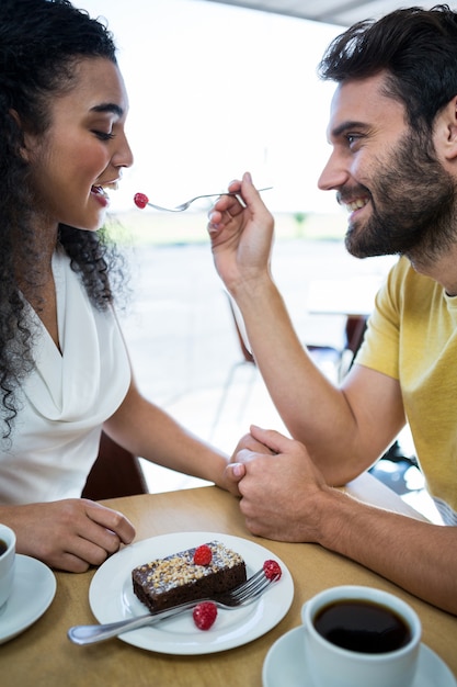 Photo man feeding pastry cherry to woman in coffee shop