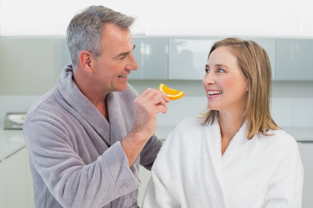 Man feeding woman orange slice in kitchen