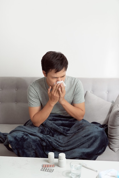 Man feeling cold, lying in the sofa and blowing his nose