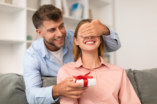 Man feliciteert vrouw, geeft geschenk, sluit haar ogen thuis.