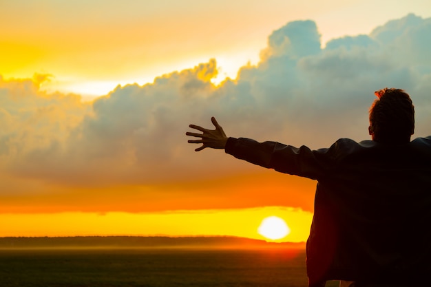 Man in field on beautiful sunset. Silhouette of young man with outstretched arms