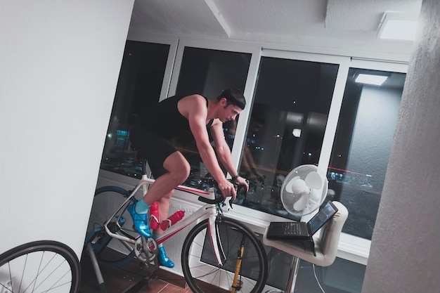 Foto man fietsen op de machine trainer hij oefent in het huis's nachts spelen online fiets racen spel