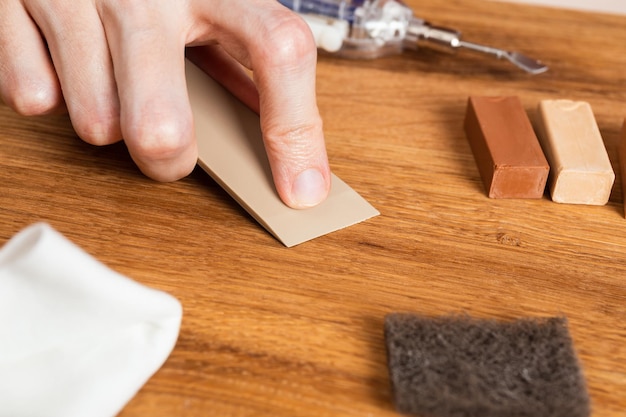 Man filling cracks scratches dents by wax in the wooden floor furniture Professional repair kit laminate or parquet with hard wax sticks Renovating surface of furniture Close up hands