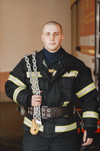 Foto uomo in uniforme antincendio. vigile del fuoco vicino all'automobile. uomo in garage