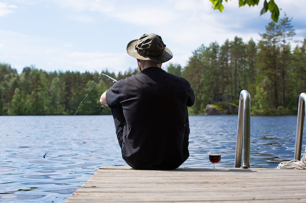 Man fishing from wooden pier near cottage on lake in Finland at summer