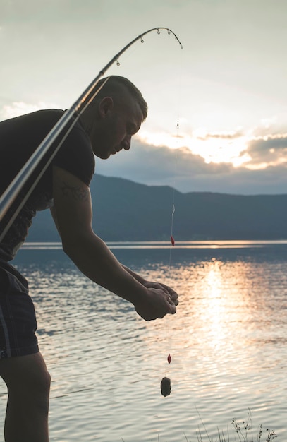 写真 夕暮れの空に向かって湖で釣りをしている男