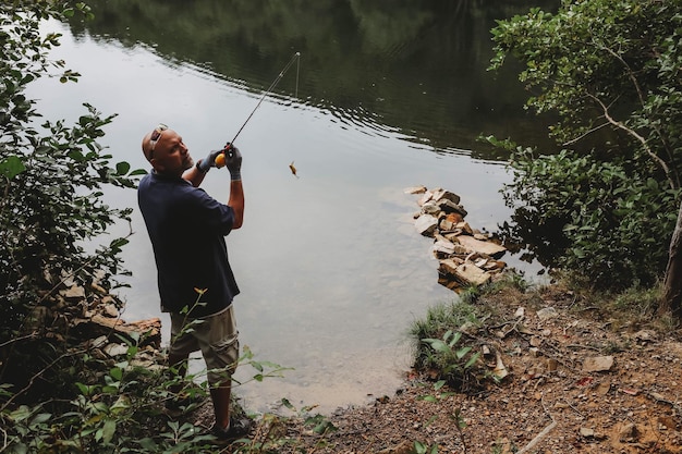 写真 樹木に逆らって湖で釣りをしている男