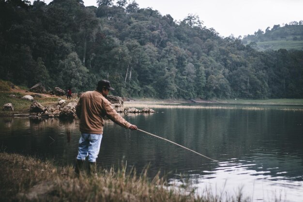 Photo man fishing in lake against trees