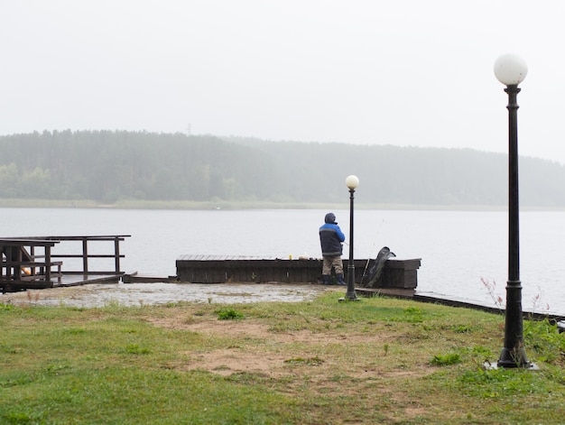 Uomo che pesca sul molo in una giornata piovosa e nebbiosa