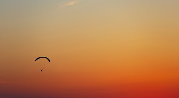 日没時の雲ひとつない空のパラグライダーでの男の飛行。