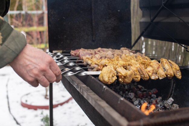 Мужчина переворачивает мясной шашлык на гриле-барбекю