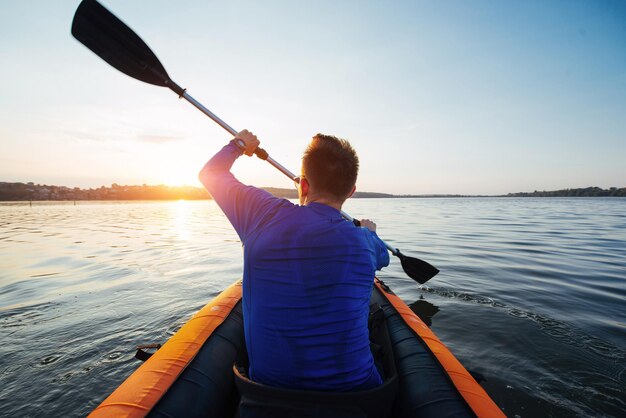 Photo man floating on lake in a kayak at fantastic sunset