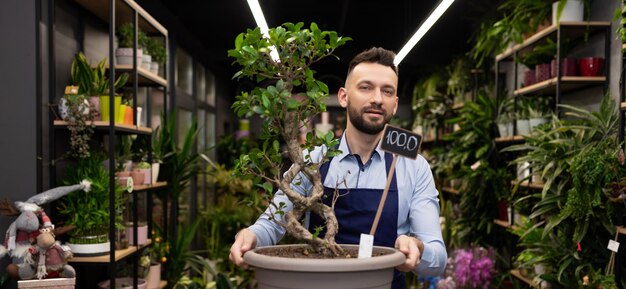 Man florist holding a pot with a small tree in his hands looking super camera