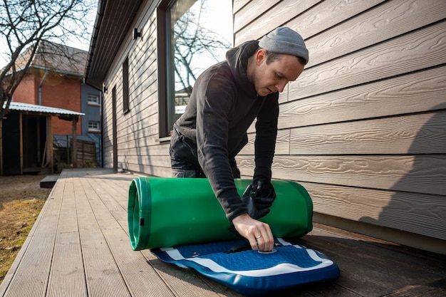 Man folding an inflatable standup paddleboard SUP on a wooden deck next to a modern home