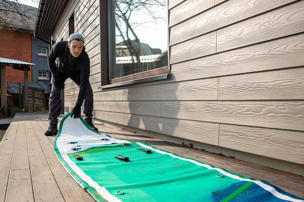 Man folding an inflatable standup paddleboard SUP on a wooden deck next to a modern home