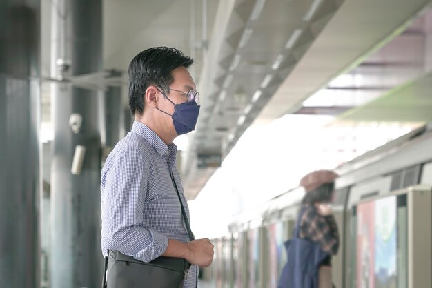 Man forens met gezichtsmasker die op het metroplatform staat te wachten om de trein in te gaan Gemaskeerd doorvoerconcept