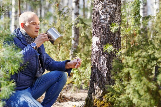 Man in forest drinking from a cup tree sap