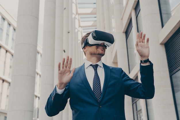 Man in formal blue suit walking around in virtual reality while wearing VR goggles