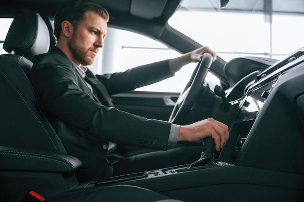 正式なビジネス服を着た男が現代の自動車に座っている