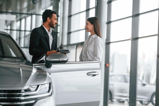 Man in formal clothes is consulting woman about the automobile in the car dealership