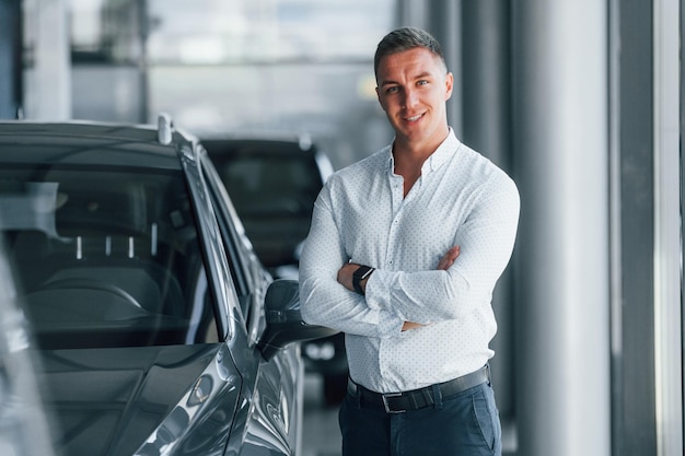 Man in formal clothes is standing indoors near moden new car