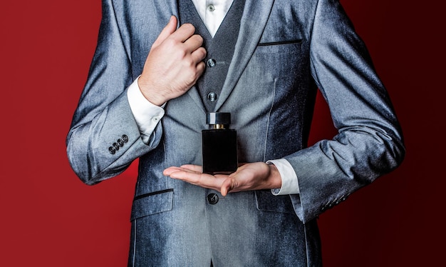 Man in formal suit bottle of perfume closeup Man holding up bottle of perfume Men perfume in the hand on suit background Fragrance smell