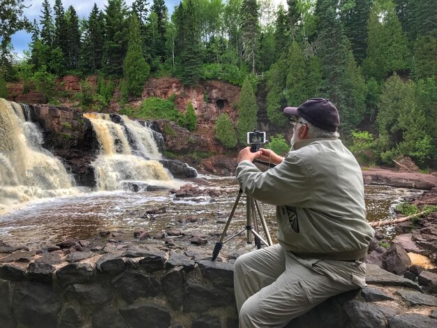 Man fotografeert waterval via mobiele telefoon met monopod terwijl hij in het bos zit