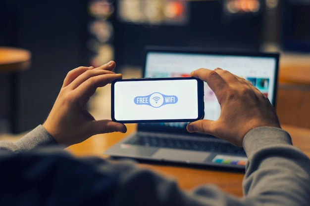 Man freelancer holds a smartphone with free internet in his hands on the background of a laptop.