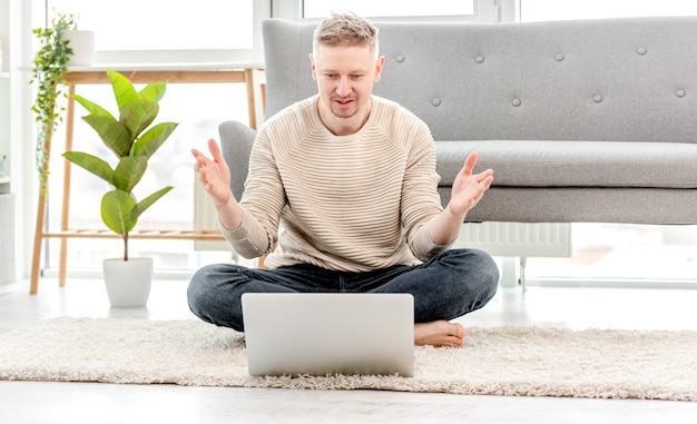 Man freelancer working at home with laptop and surprised holding his hands up