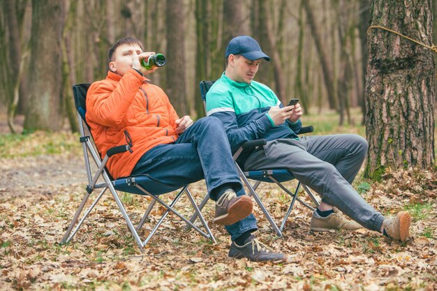 椅子に座って話している男の友人は、森で休んでいるクマを飲みます