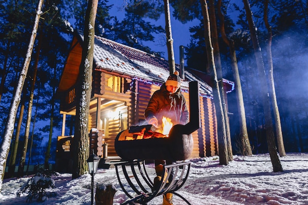 Un uomo frigge carne alla griglia contro il cottage la sera e nel fumo