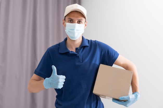 Uomo del servizio di consegna in t-shirt, in maschera protettiva e guanti che danno ordine di cibo e tengono scatole su sfondo bianco.