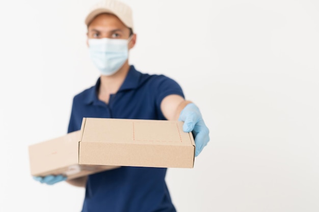 Man from delivery service in t-shirt, in protective mask and gloves giving food order and holding boxes over white background.