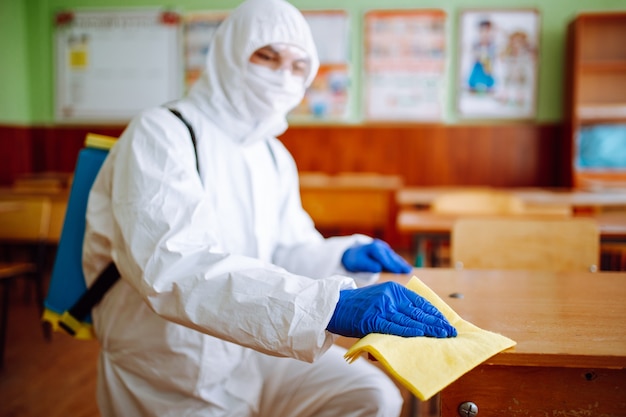 A man from disinfection group cleans up the desk at school with a yellow rag. Professional worker sterilizes the classroom to prevent covid-19 spread. Healthcare of pupils and students concept.