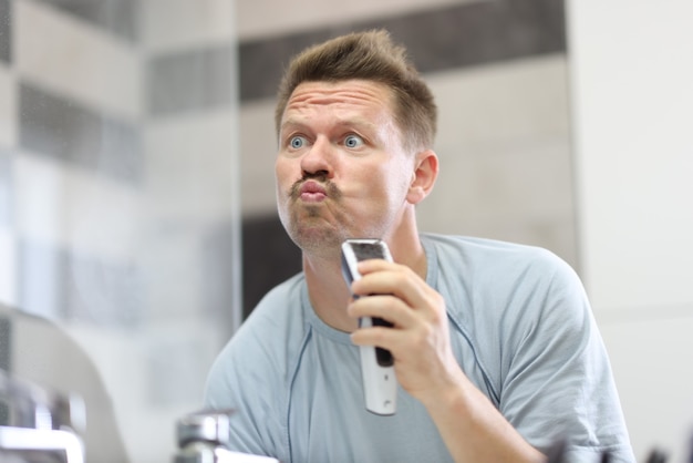 Man in front of a mirror shaves off his stubble with machine