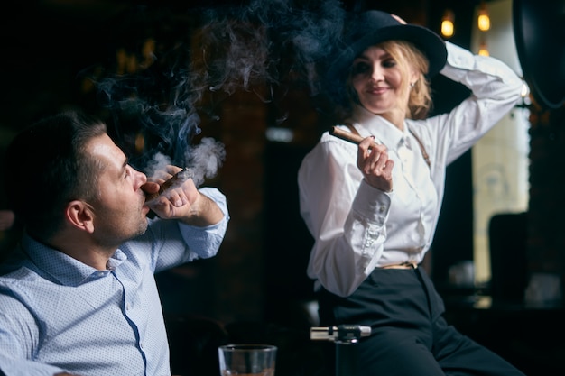 Foto l'uomo-gangster e la bella donna anziana che fumano sigari in un bar