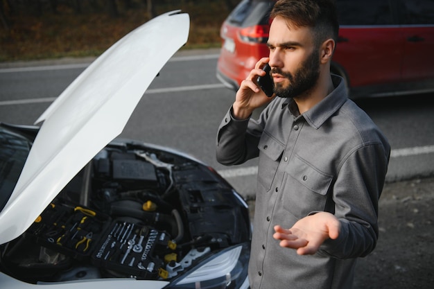 Man gebruikt een gsm-oproepgarage voor de open motorkap van een kapotte auto op de weg in het bos Autopech concept