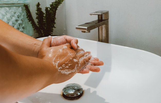 Man gebruikt zeep en wast handen onder de waterkraan voor Covid 19-viruspreventie. Concept tot hygiëne om verspreiding van Covid 19 en Hygiënehanddetail te stoppen.