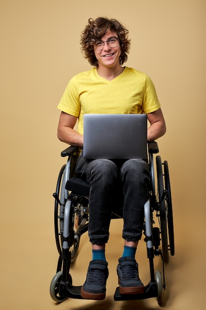 Man gehandicapte student voorbereiden op examen met behulp van laptop, zittend op een rolstoel geïsoleerd in de studio. portret. online onderwijs voor gehandicapten