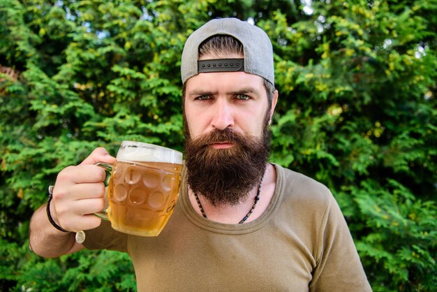 Man genieten van bier in de zomer. Alcohol en barconcept. Creatieve jonge brouwer. Ambachtelijk bier is jong, stedelijk en modieus. Aparte biercultuur. Hipster brutale bebaarde man houdt mok koud vers bier.