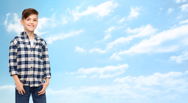 man, geslacht, jeugd, mode en mensen concept - lachende jongen in geruit overhemd en spijkerbroek over blauwe lucht en wolken achtergrond