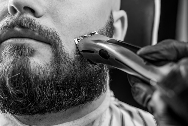 Man getting his beard trimmed with electric razor in barbershop black and white image