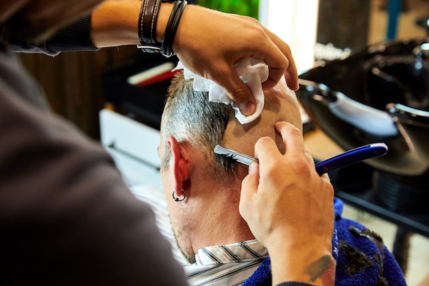 man getting shaved with straight edge razor by hairdresser at barbershop 