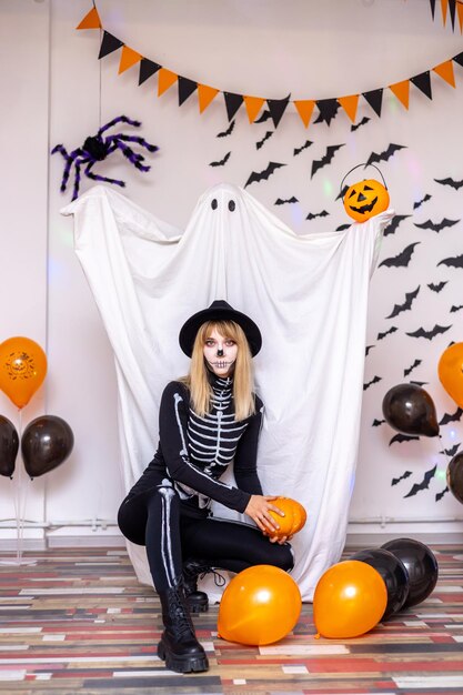 A man in a ghost costume and a woman in a skeleton costume on a decorated background with balls and pumpkins on a Halloween holiday