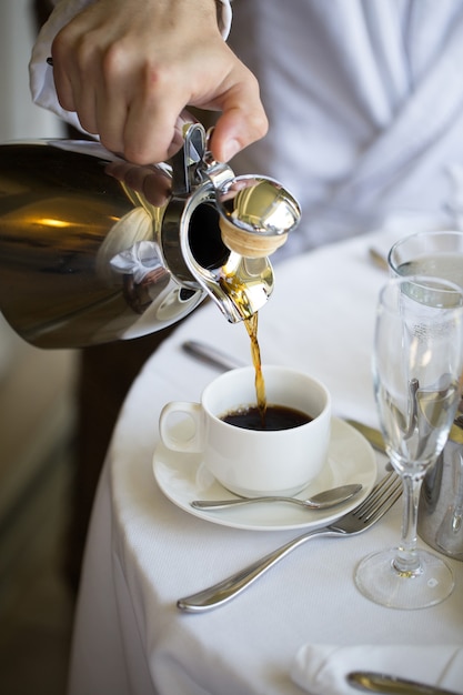 Man giet koffie in een witte kop