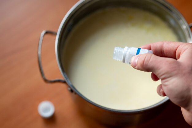 Man giet zuurdeeg voor yoghurt uit in de pan met melk Yoghurt maken thuis