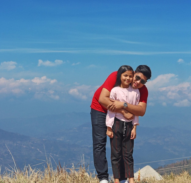 A man and a girl are standing in a field and the sky is blue with clouds.